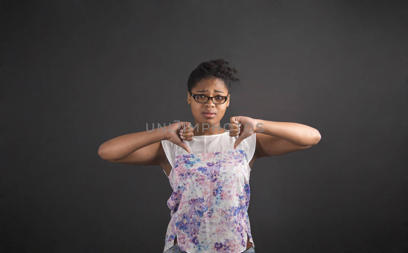 South African or African American black woman teacher or student with thumbs down hand signal on a chalk black board background inside