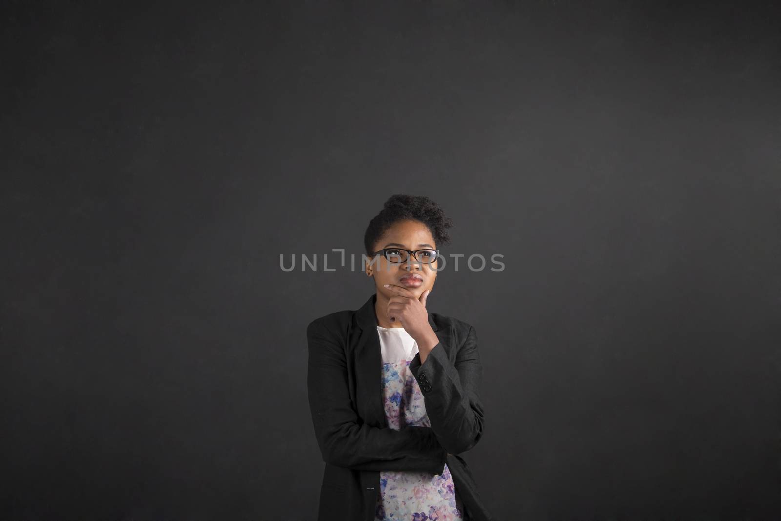 South African or African American black woman teacher or student with her hand on her chin whilst thinking standing against a chalk black board background inside
