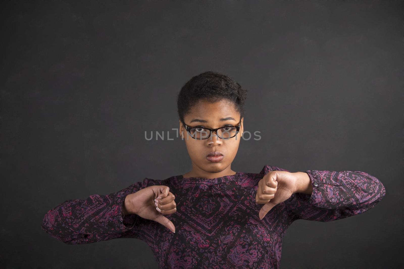 South African or African American black woman teacher or student with thumbs down hand signal on a chalk black board background inside