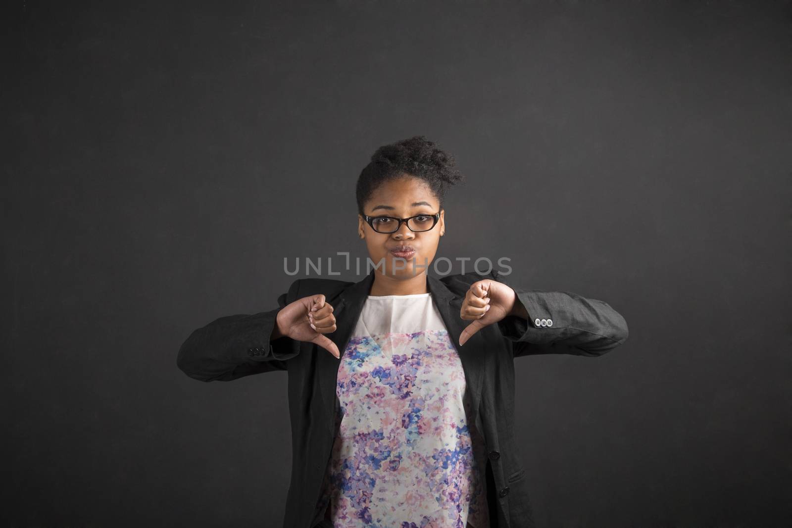 African woman with thumbs down hand signal on blackboard background by alistaircotton