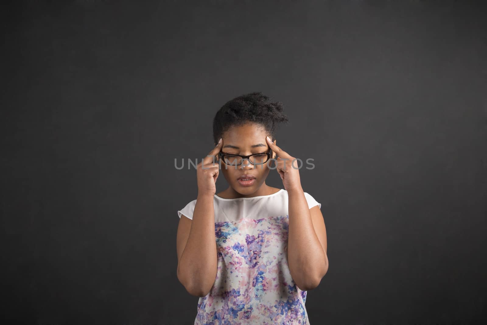 African woman with fingers on temples thinking on blackboard background by alistaircotton