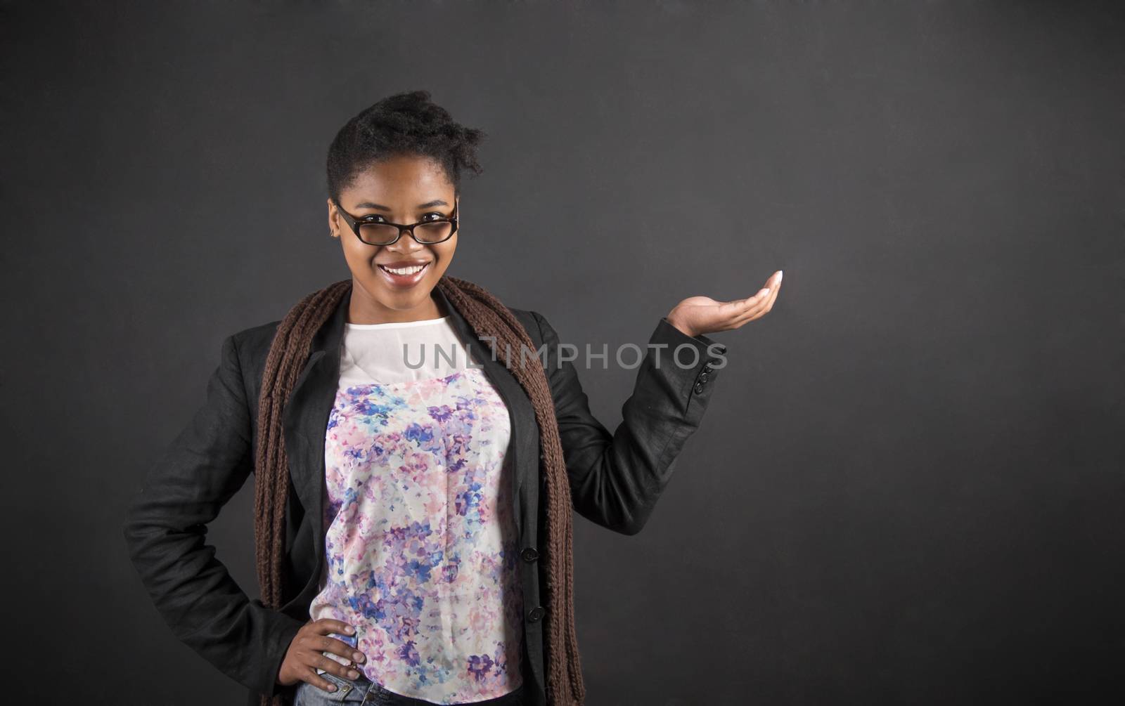 South African or African American black woman teacher or student holding her hand out to the side standing against a chalk blackboard background inside