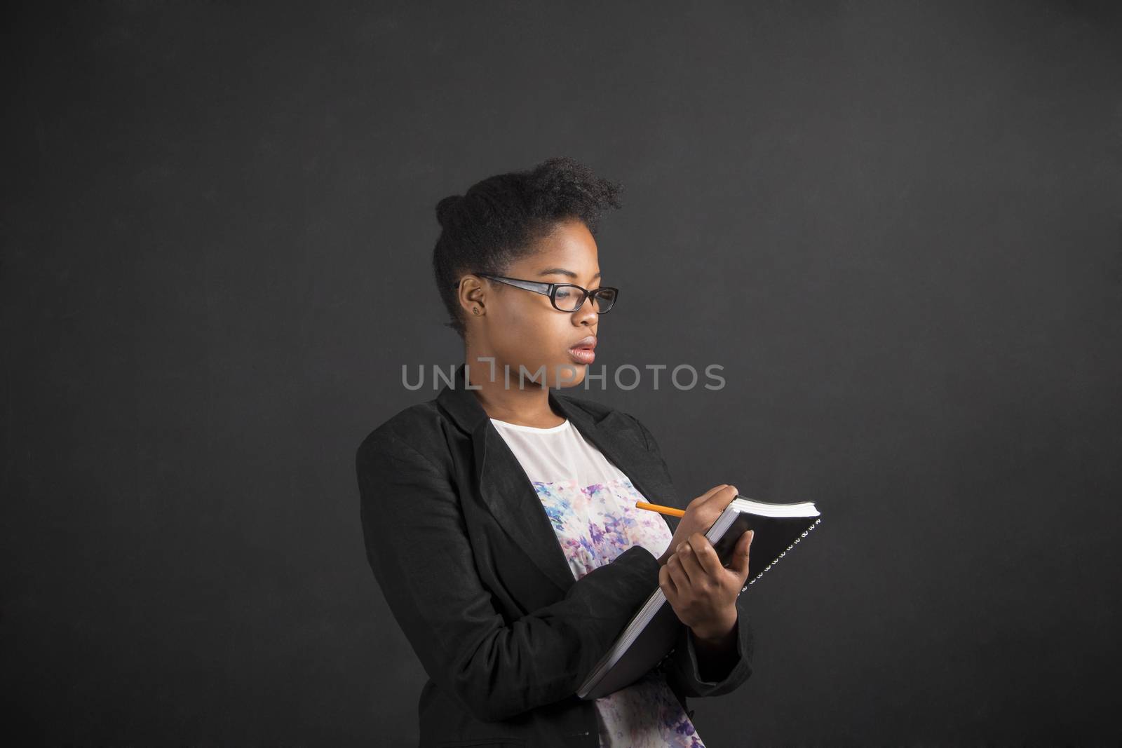 African woman writing in book diary on blackboard background by alistaircotton