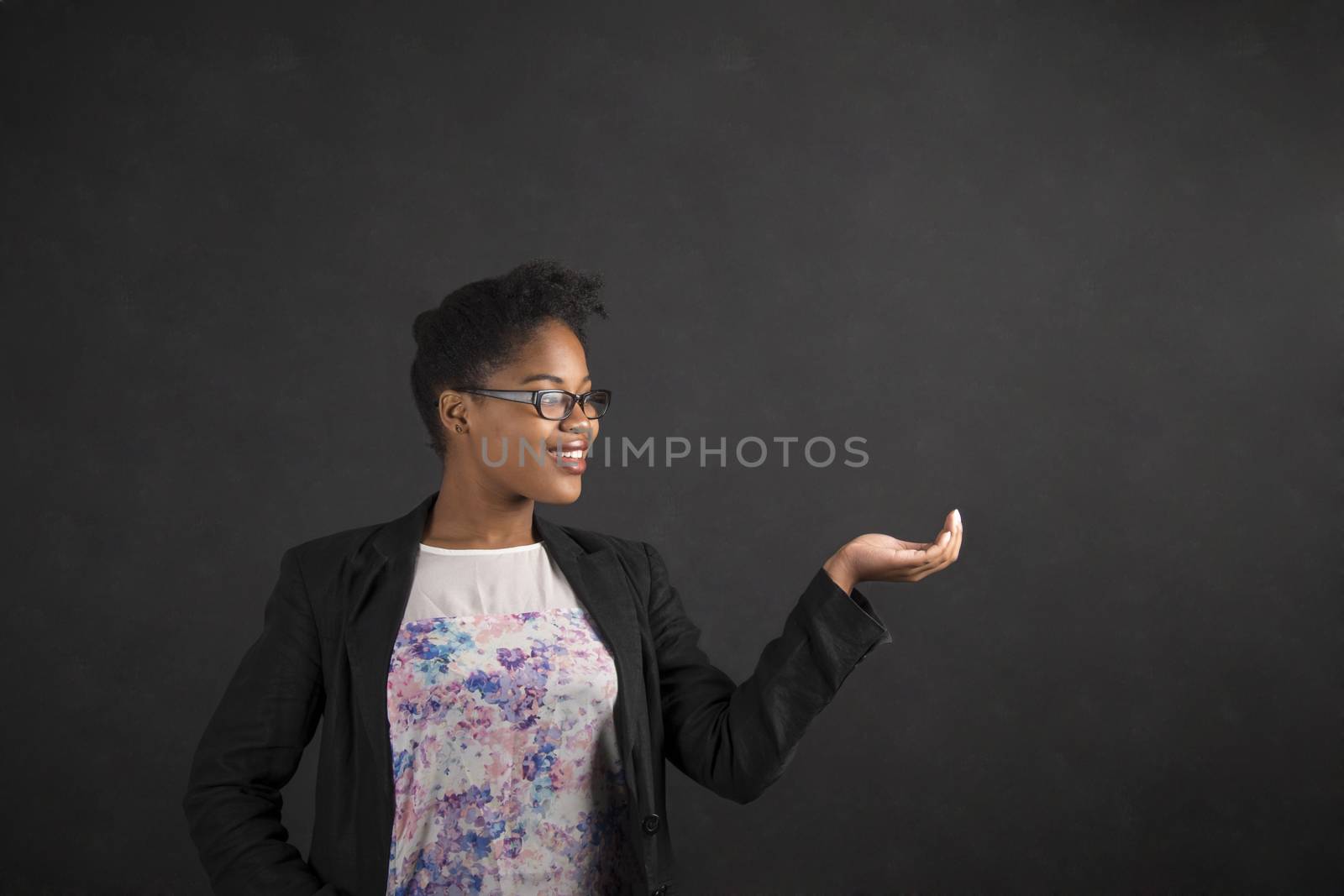 South African or African American black woman teacher or student holding her hand out to the side looking at it standing against a chalk blackboard background inside