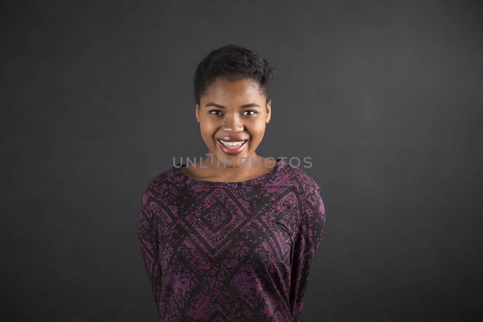 South African or African American woman teacher or student with arms behind back on chalk black board background