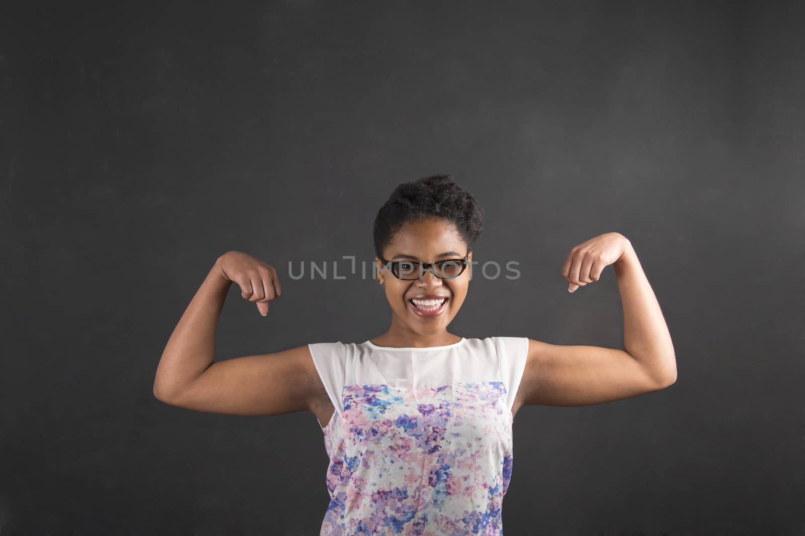 South African or African American black woman teacher or student with strong muscular arms standing against a chalk blackboard background inside