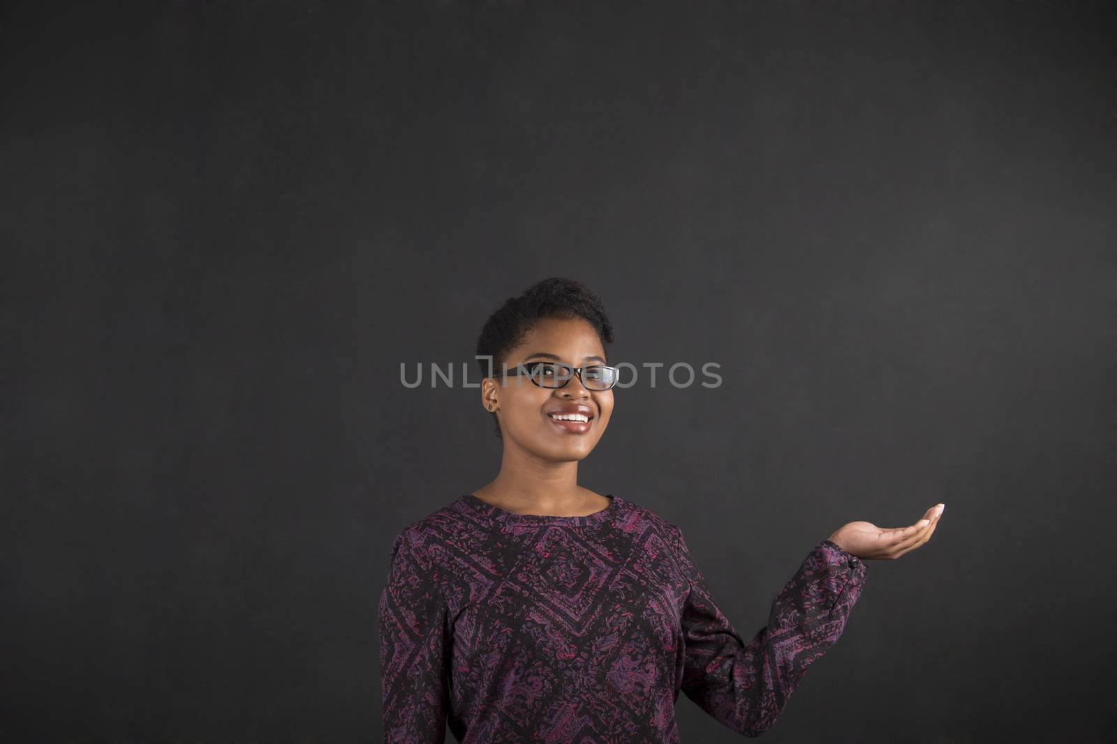 South African or African American black woman teacher or student holding her hand out to the side standing against a chalk blackboard background inside