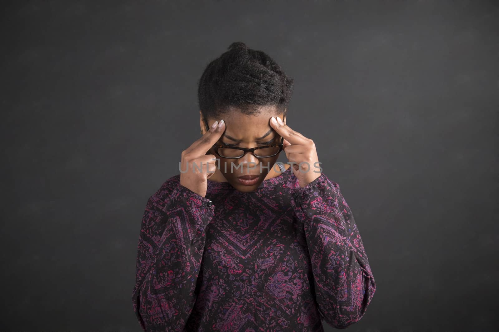South African or African American black woman teacher or student holding her fingers on her temples thinking against a chalk black board background inside