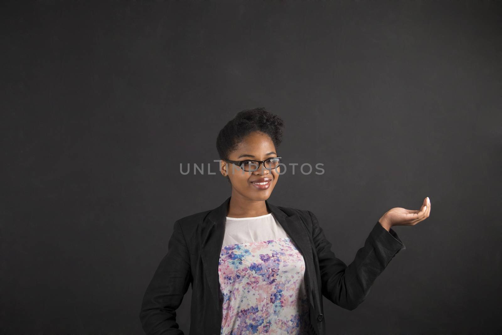 African woman holding hand out on blackboard background by alistaircotton