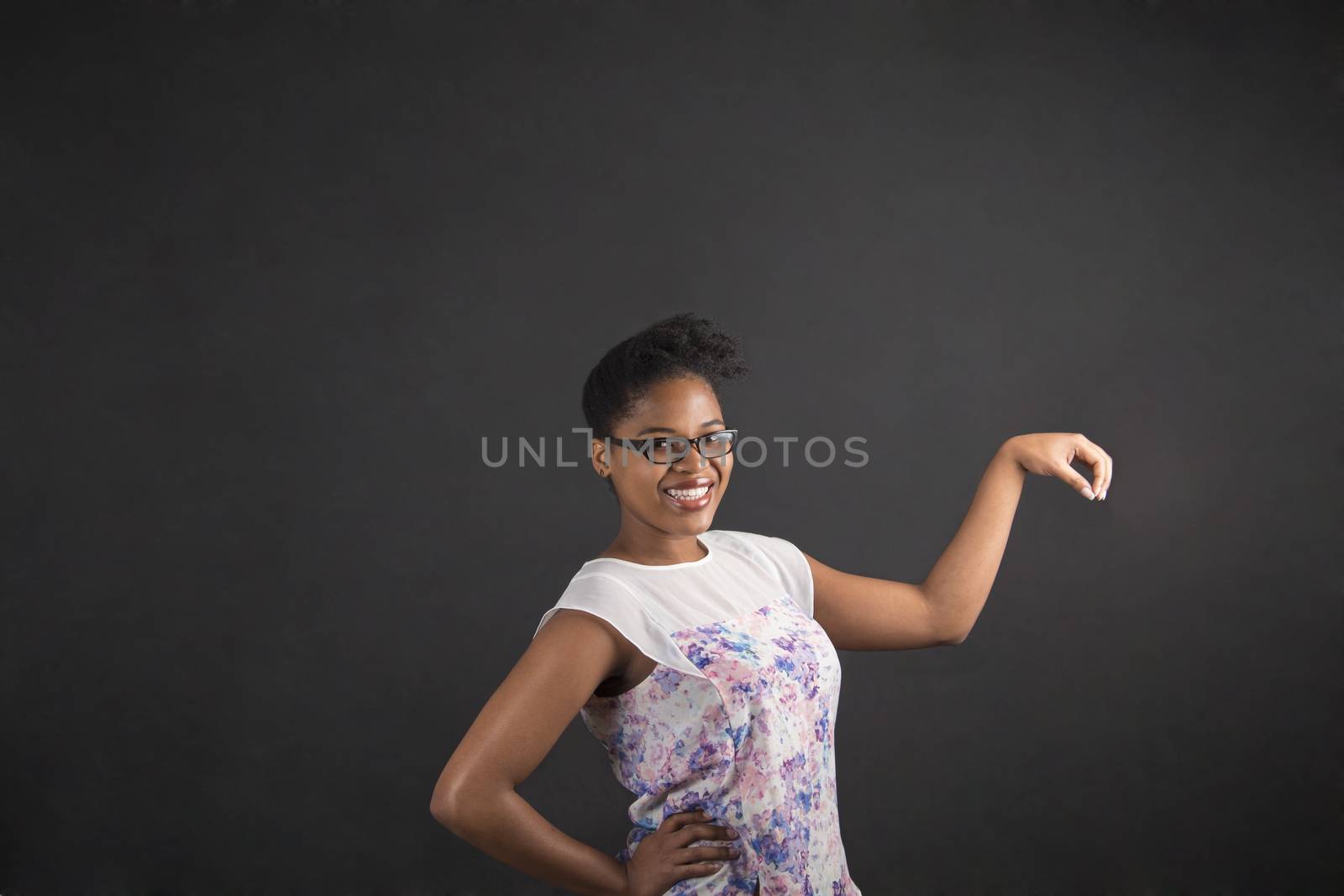 South African or African American woman teacher or student holding object out to the side on chalk black board background