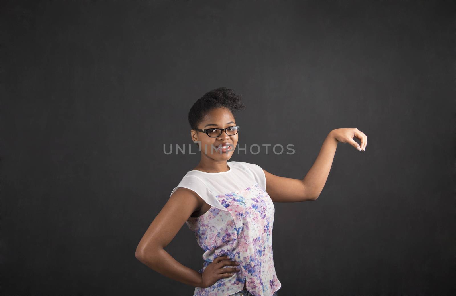 South African or African American black woman teacher or student holding an object out to her side standing against a chalk blackboard background inside