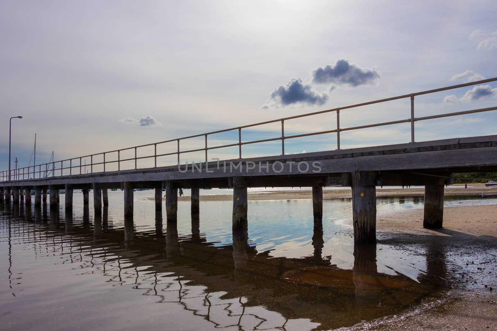 A long wooden jetty with the tide out. Boats just visible in the background.