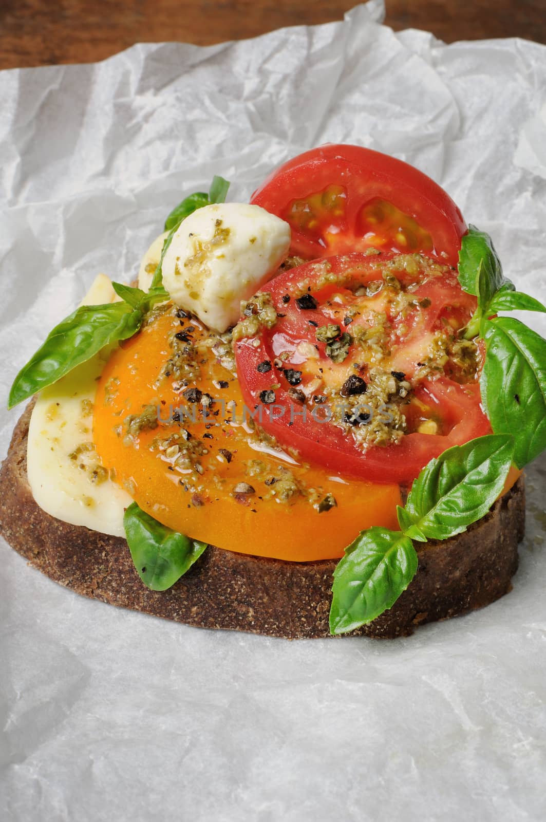 sandwich of rye bread mozzarella, tomato and pesto wrapped in baking paper