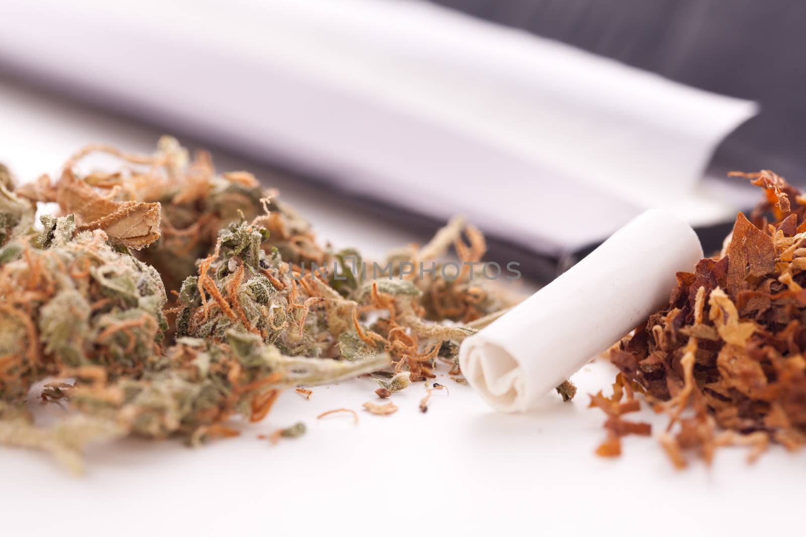 Close up Dried Cannabis Leaves on a Resealable Cellophane Wrapper and a Rolling Paper with Filter on Top of the Table