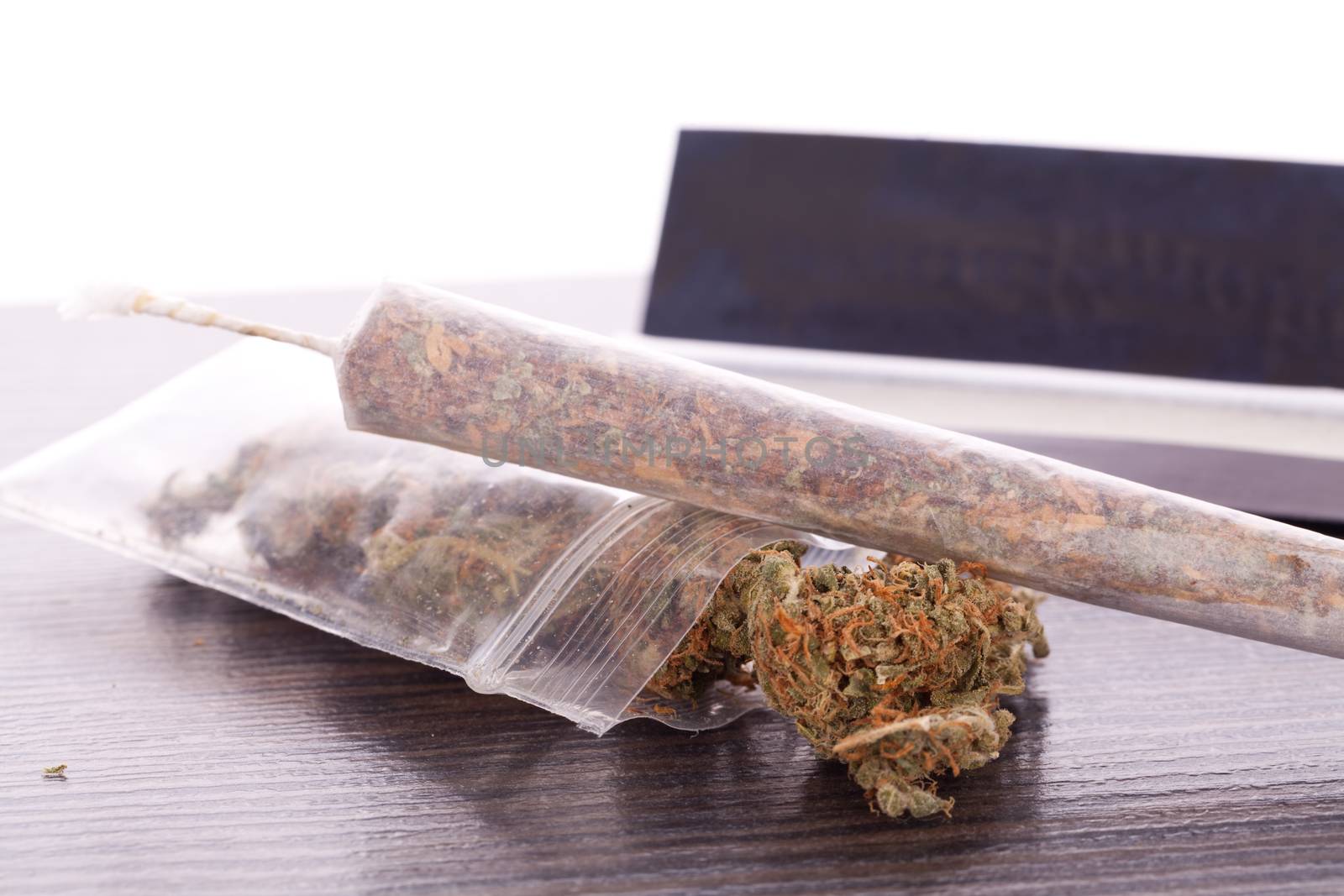 Close up Dried Cannabis Leaves on a Resealable Cellophane Wrapper and a Rolling Paper with Filter on Top of the Table