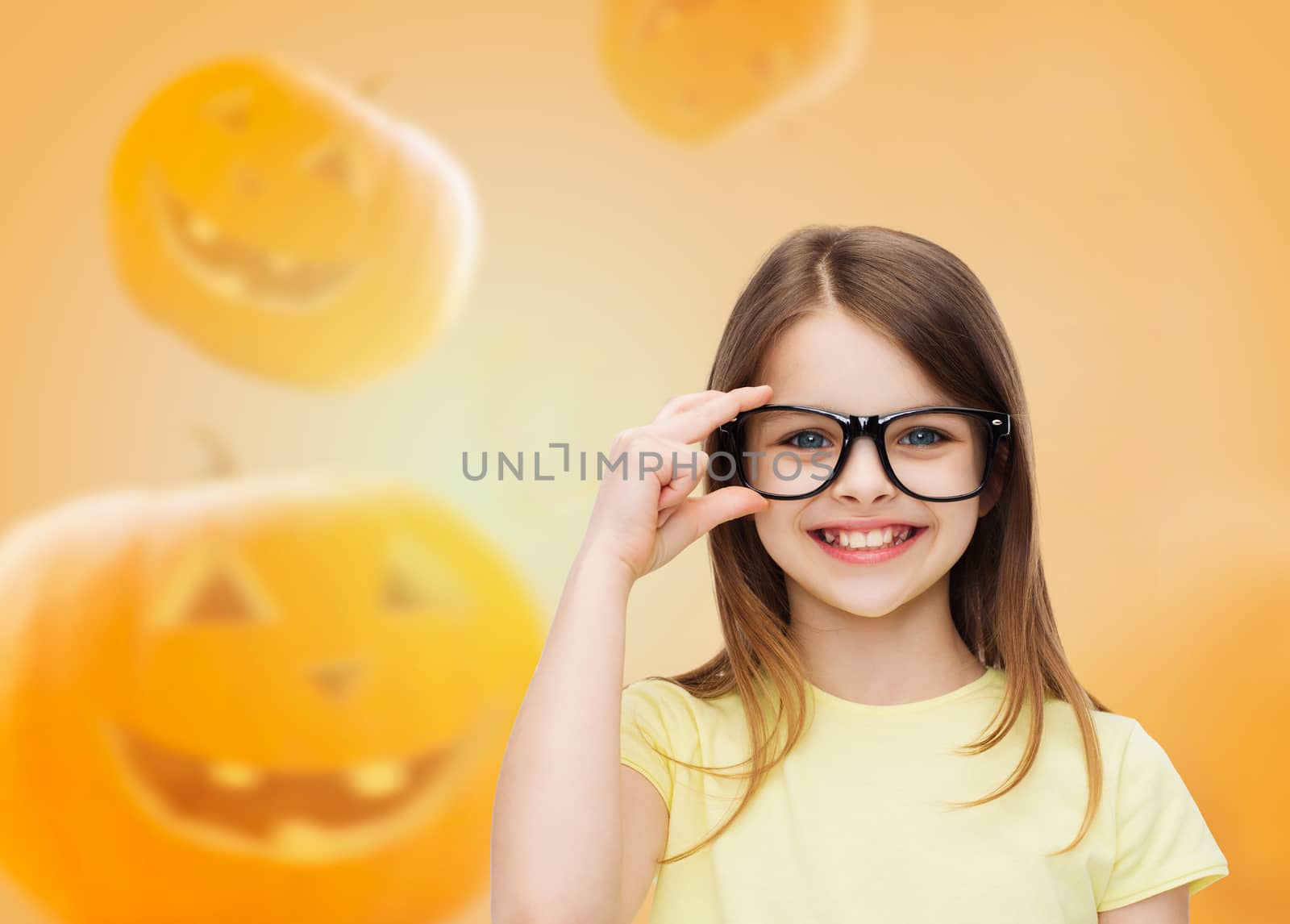 education, holidays, childhood, vision and people concept - smiling little girl in glasses over halloween pumpkins background