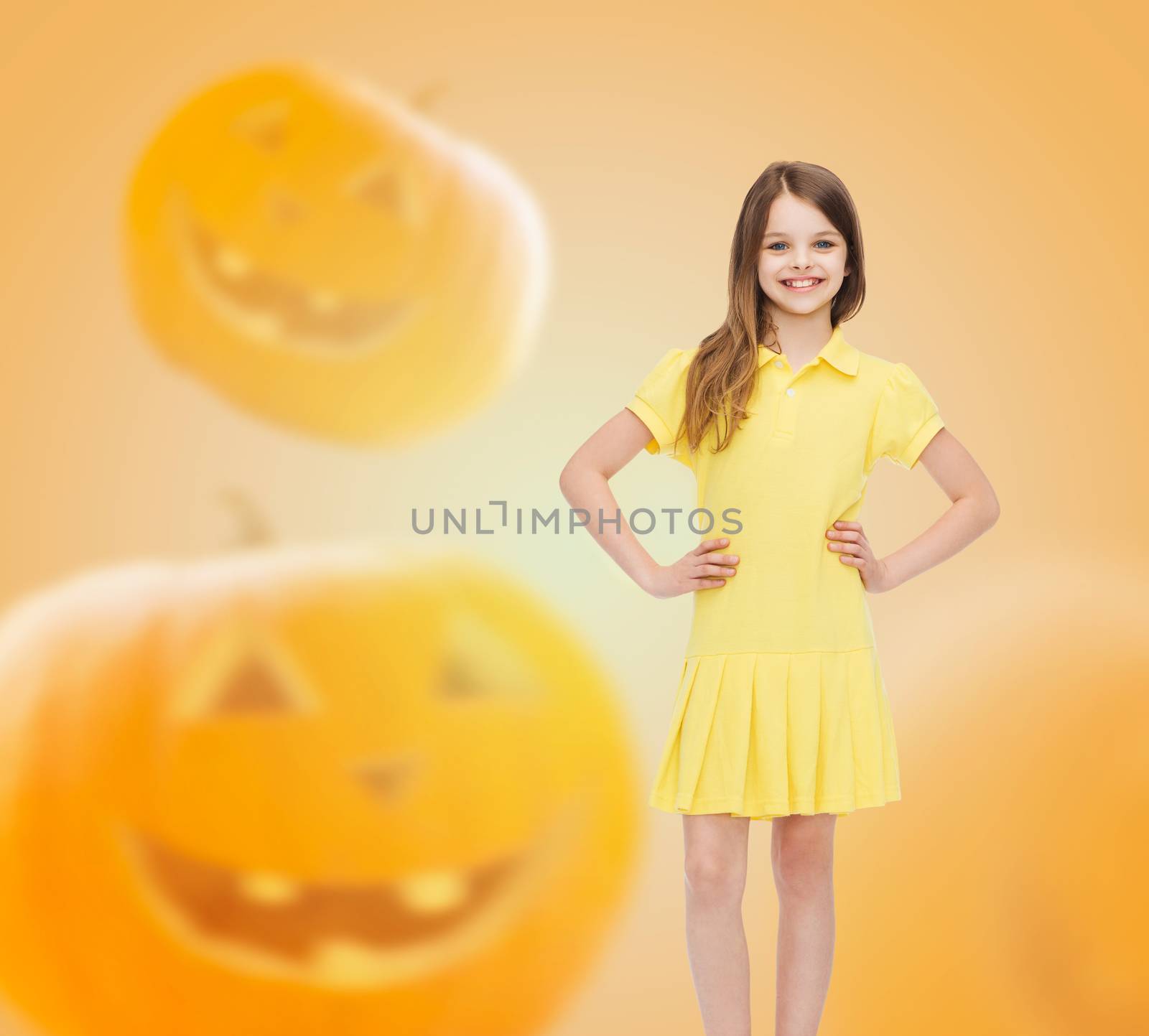 holidays, childhood, happiness and people concept - smiling little girl in dress over halloween pumpkins background