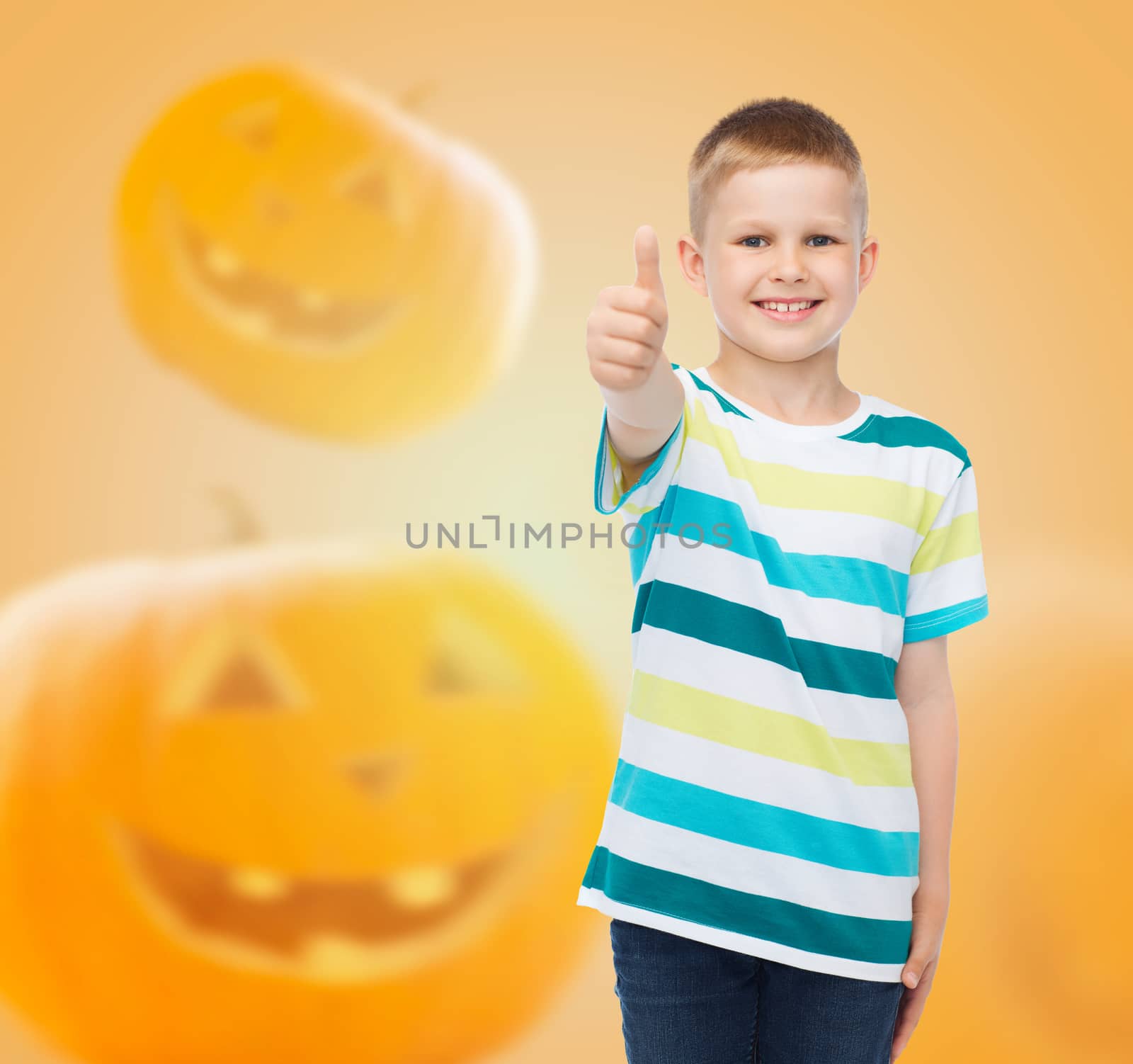 holidays, childhood, happiness, gesture and people concept - smiling little boy showing thumbs up over halloween pumpkins background