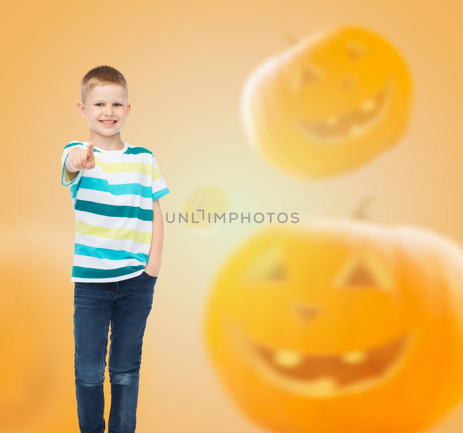holidays, childhood, happiness, gesture and people concept - smiling little boy pointing finger at you over halloween pumpkins background