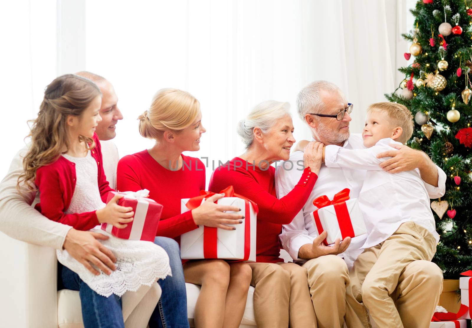 family, holidays, generation, christmas and people concept - smiling family with gift boxes sitting on couch at home