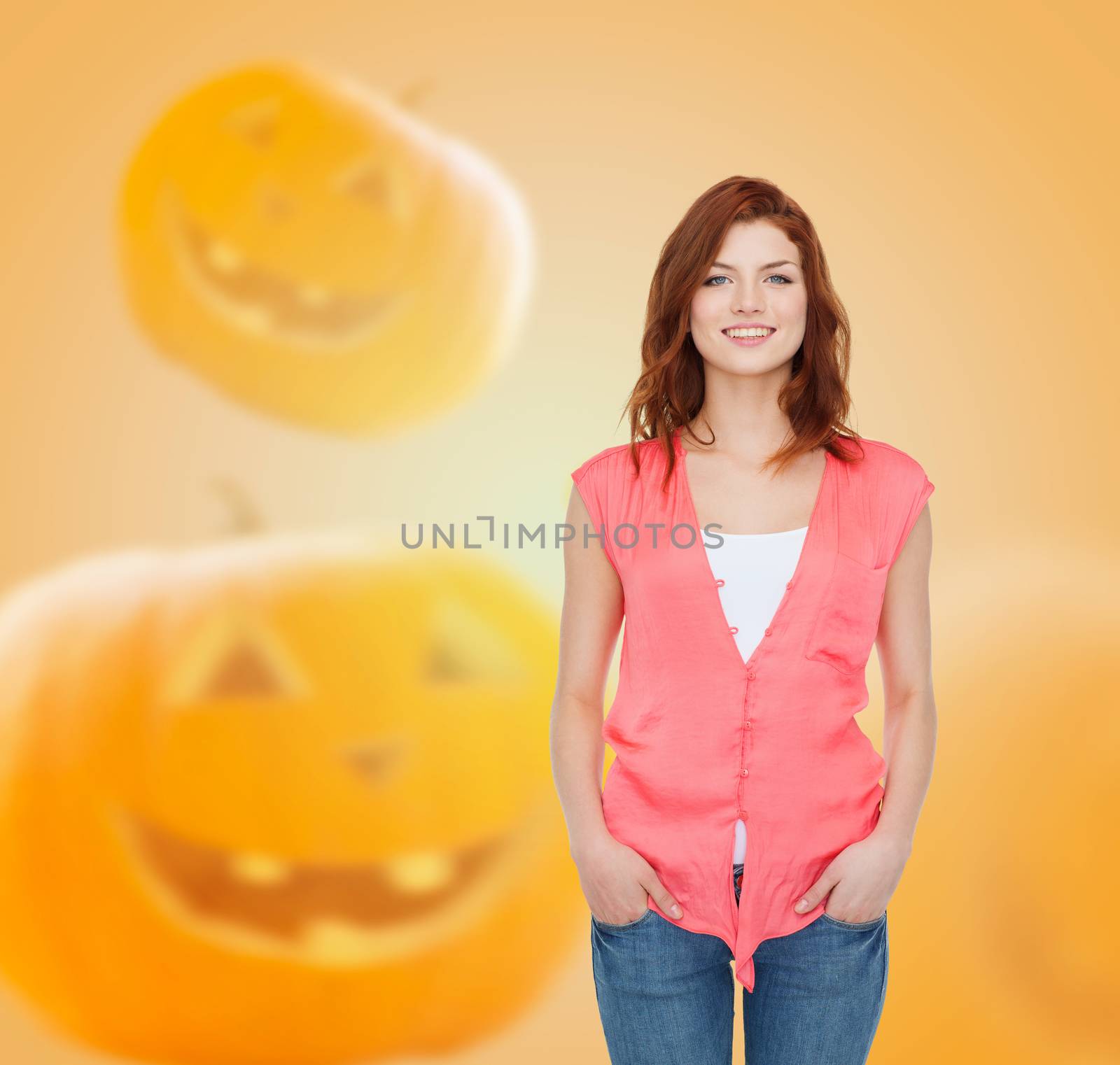 happiness, holidays and people concept - smiling teenage girl in casual clothes over halloween pumpkins background