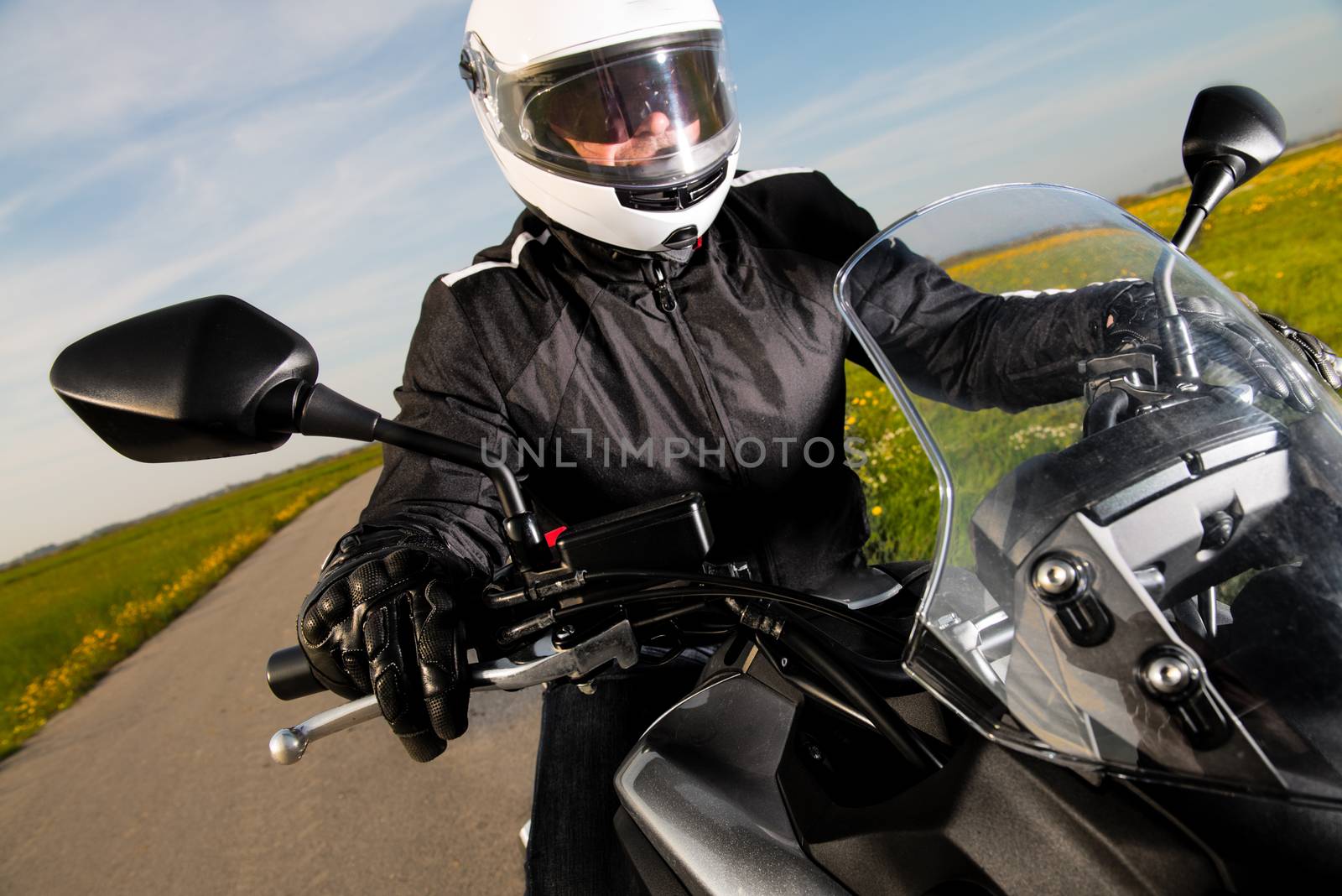 Biker in helmet and leather jacket riding on the road.