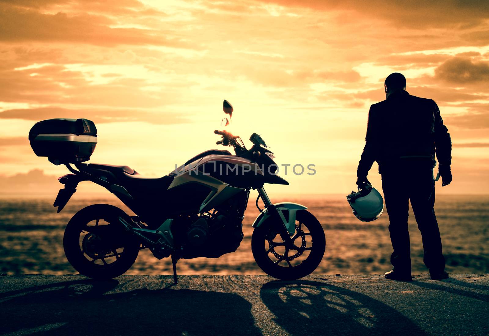 Biker standing with its motorbike on a misty sunset.