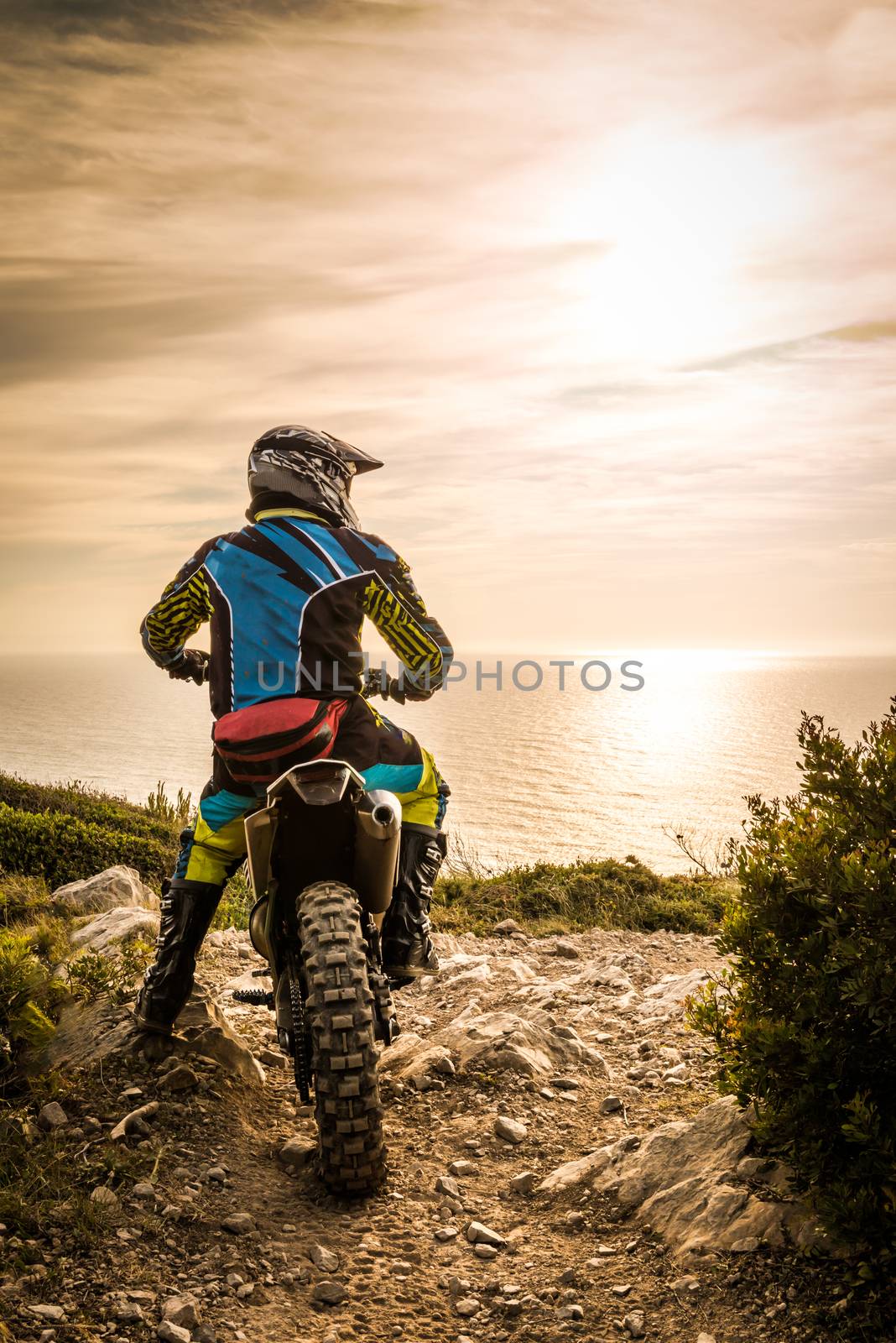 Enduro racer sitting on his motorcycle watching the sunset.