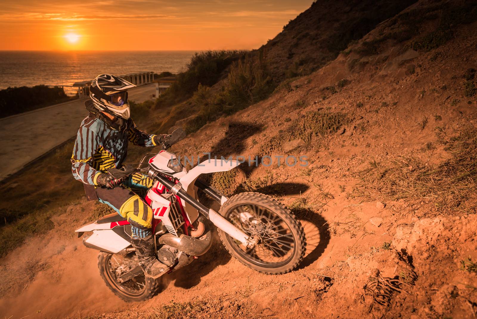 enduro rider climbing a steep slope against a beautiful sunset on a seascape