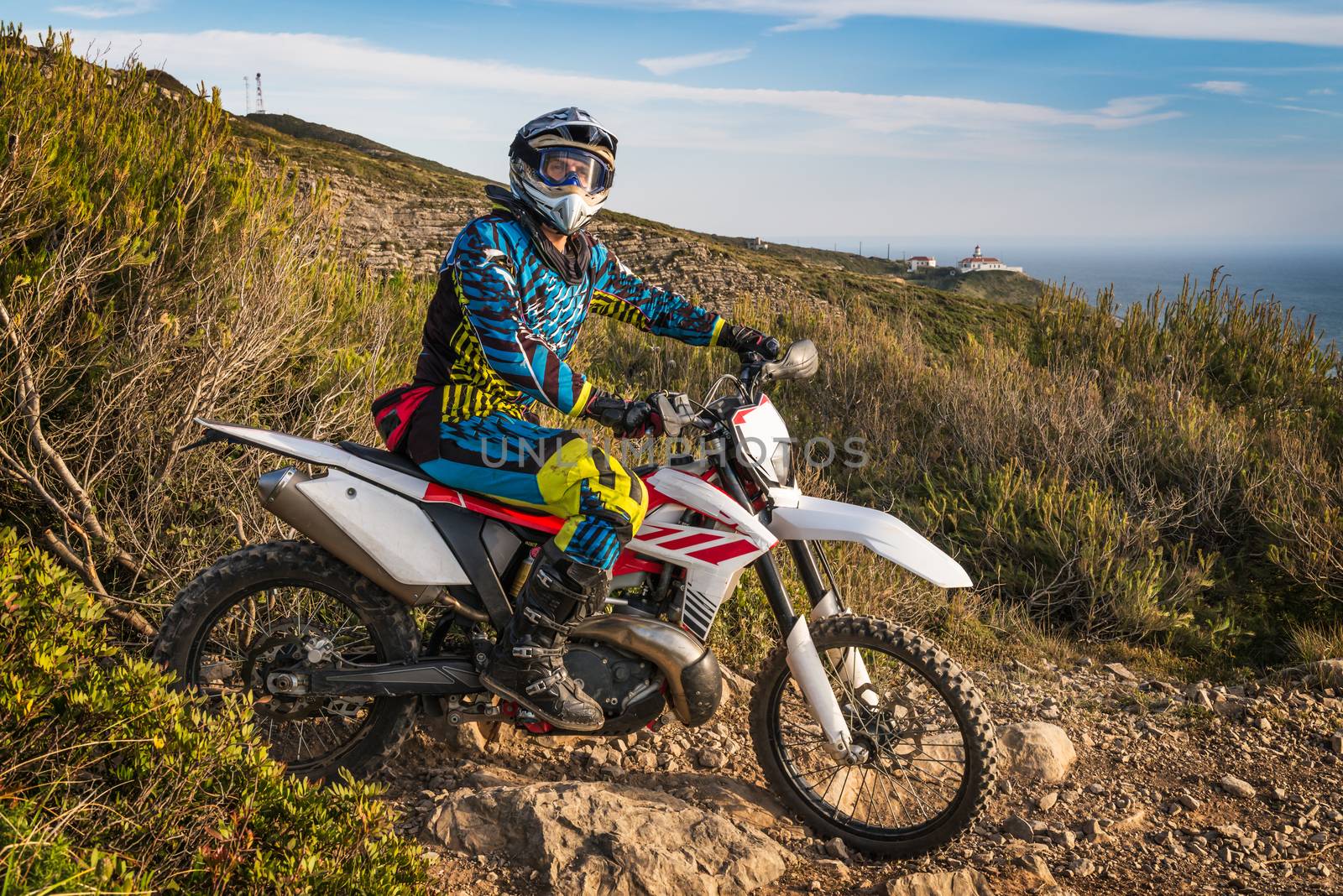 Enduro racer sitting on his motorcycle watching the sea scape on the top of the cliff.