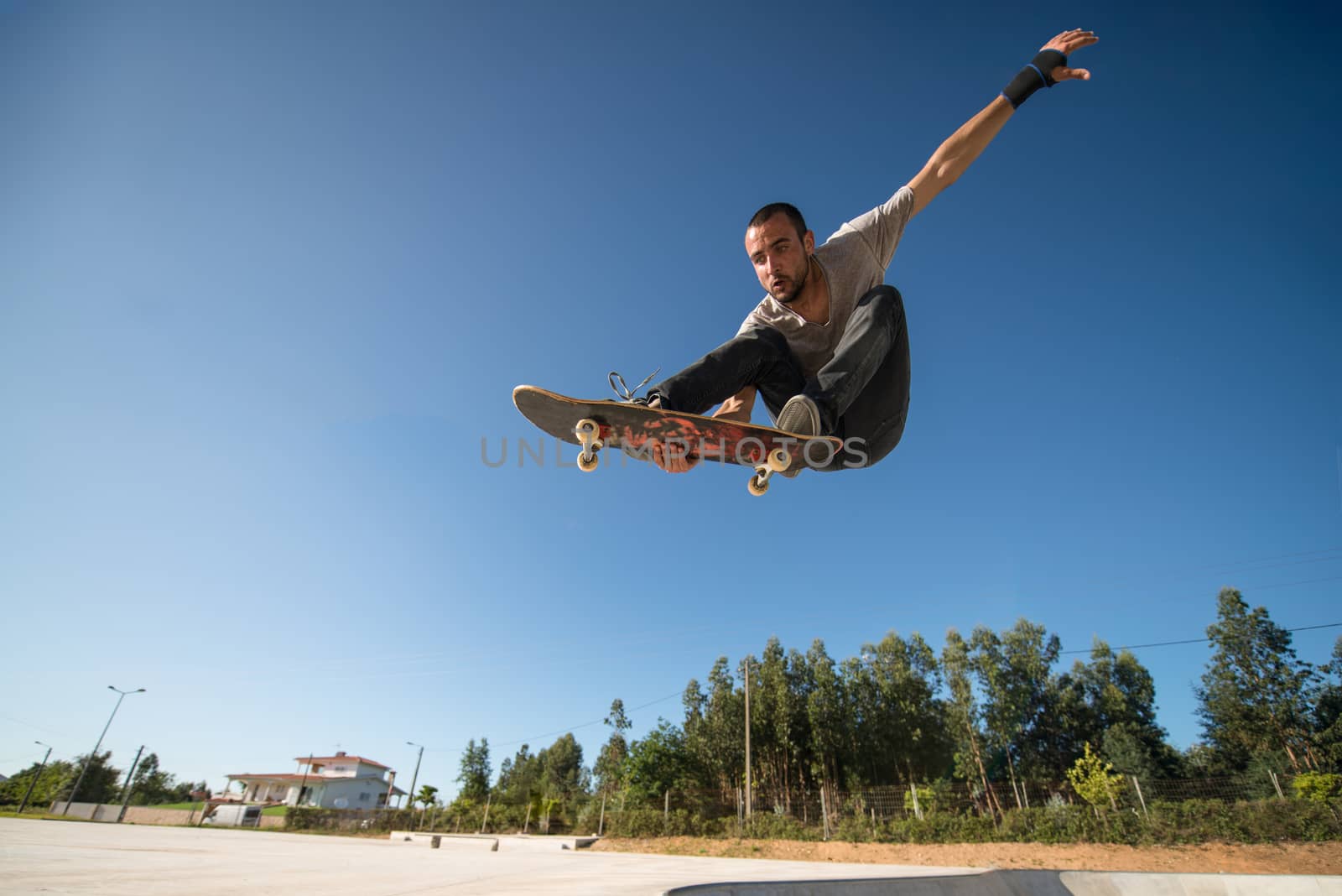 Skateboarder flying over a ramp on blue clear sky.