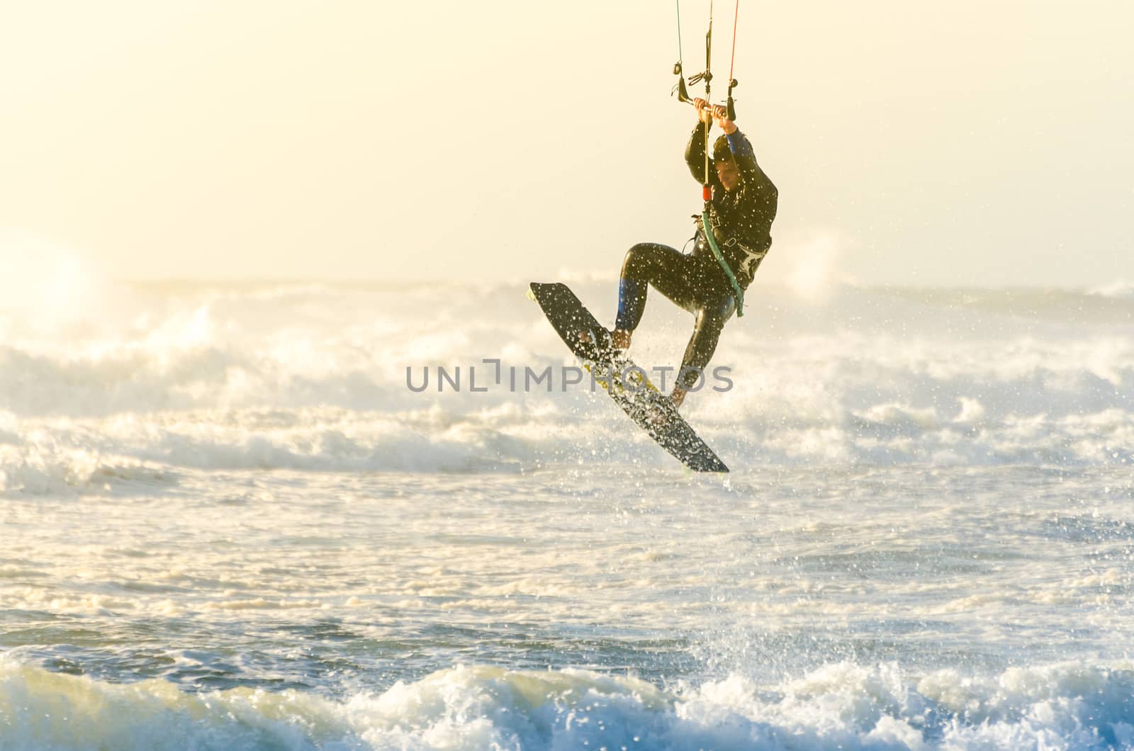 Kitesurfer jumping on a beautiful background of spray during the sunset.