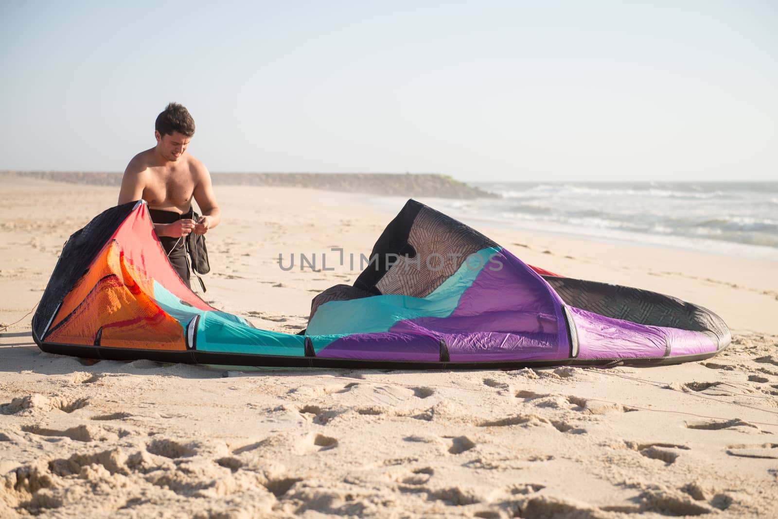 Kitesurfer prepating his equipment on a beautiful sunset at the beach.