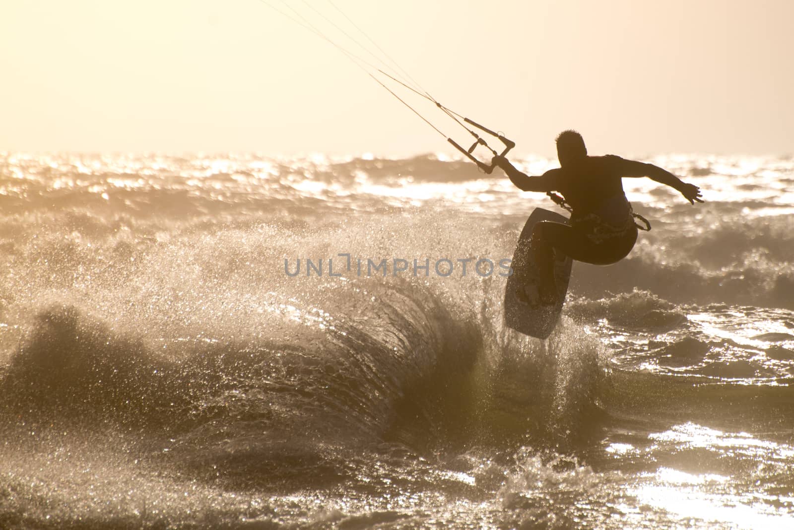 Kitesurfer jumping on a beautiful background of spray during the sunset.