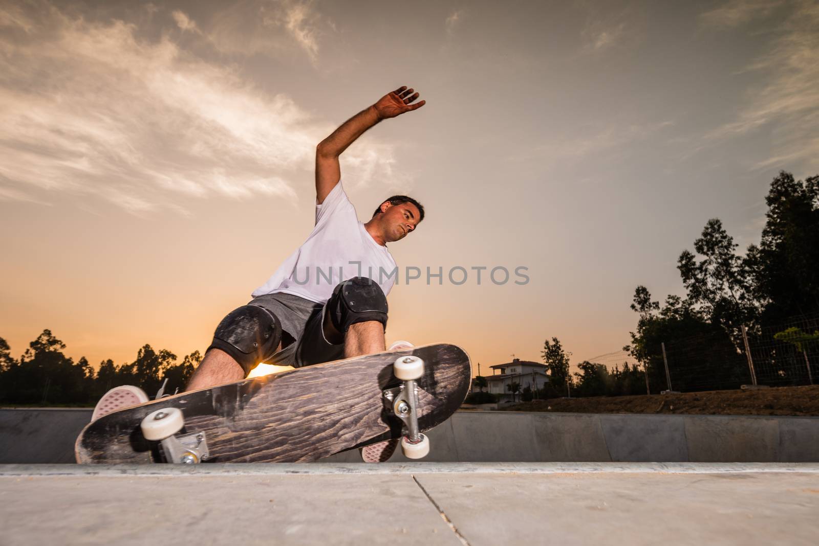 Skateboarder in a concrete pool at skatepark on a beatiful sunset.