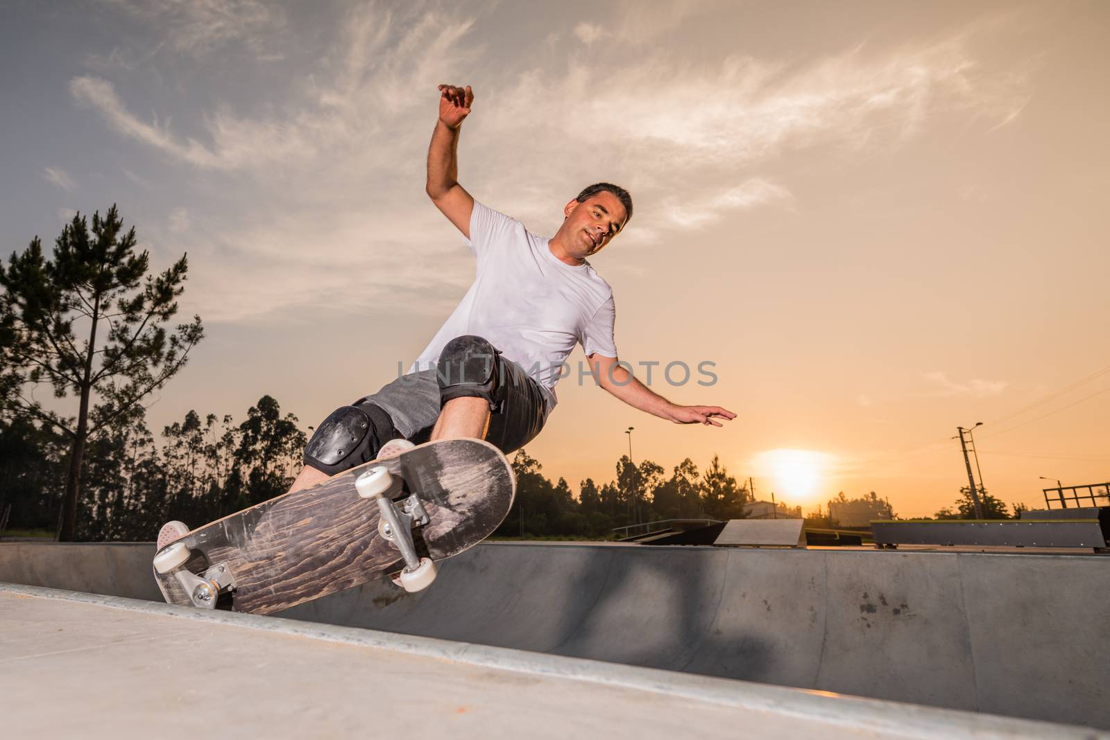 Skateboarder in a concrete pool at skatepark on a beatiful sunset.