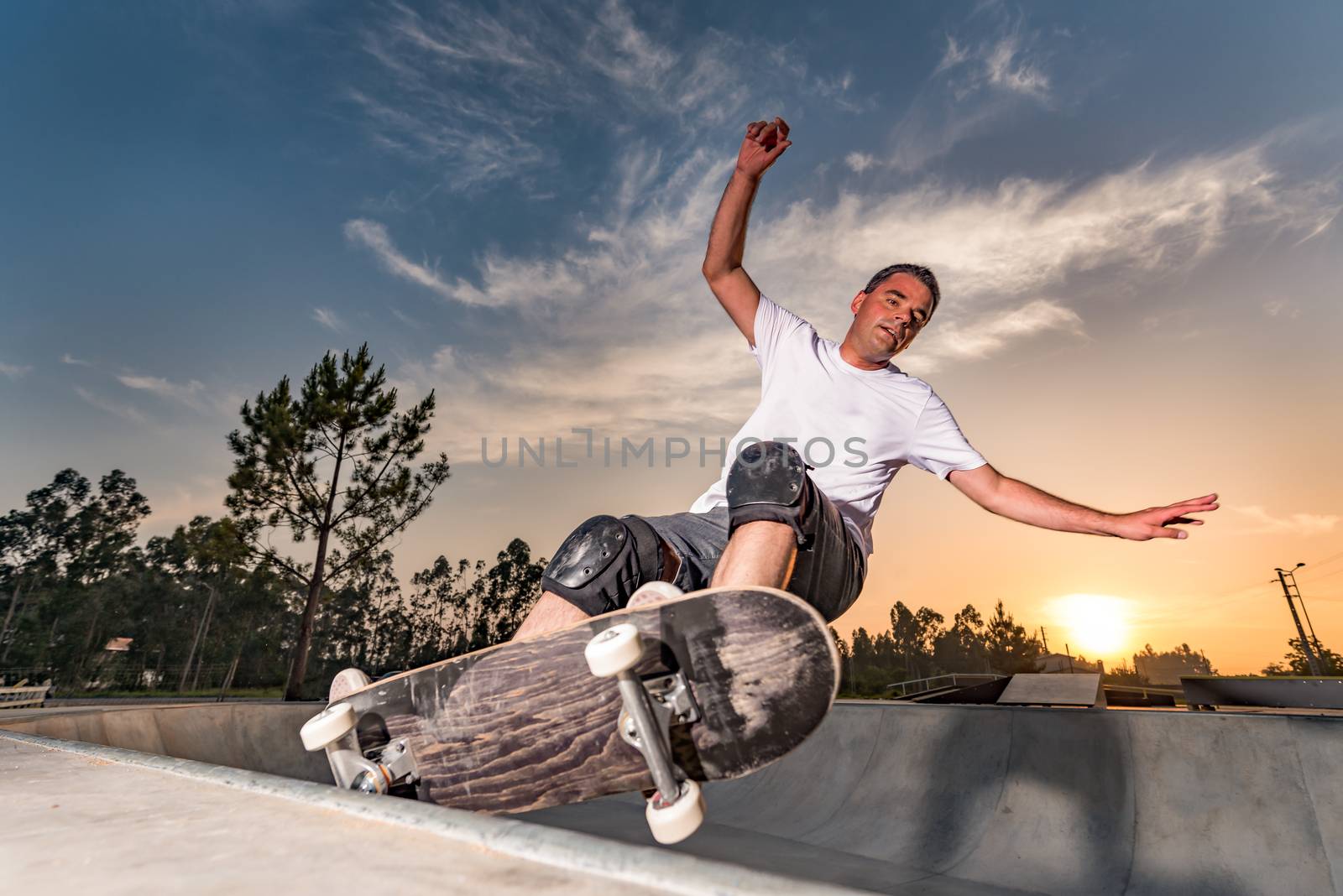 Skateboarder in a concrete pool at skatepark on a beatiful sunset.