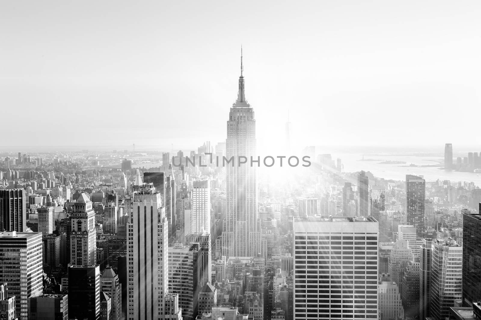 New York City. Manhattan downtown skyline with illuminated Empire State Building and skyscrapers at sunset. Vertical composition. Sunbeams and lens flare. Black and white image.