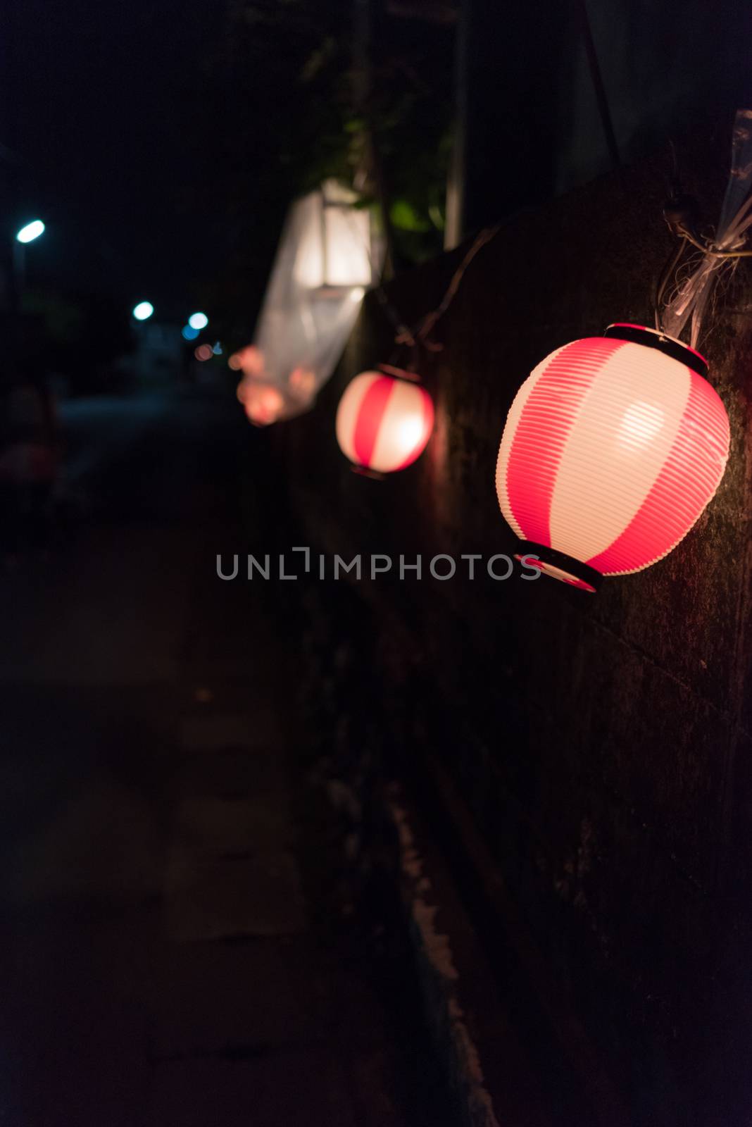 Red and white Japanese lanterns hanging along a stone wall in the dark near a summer festival in the countryside of Kochi, Japan.