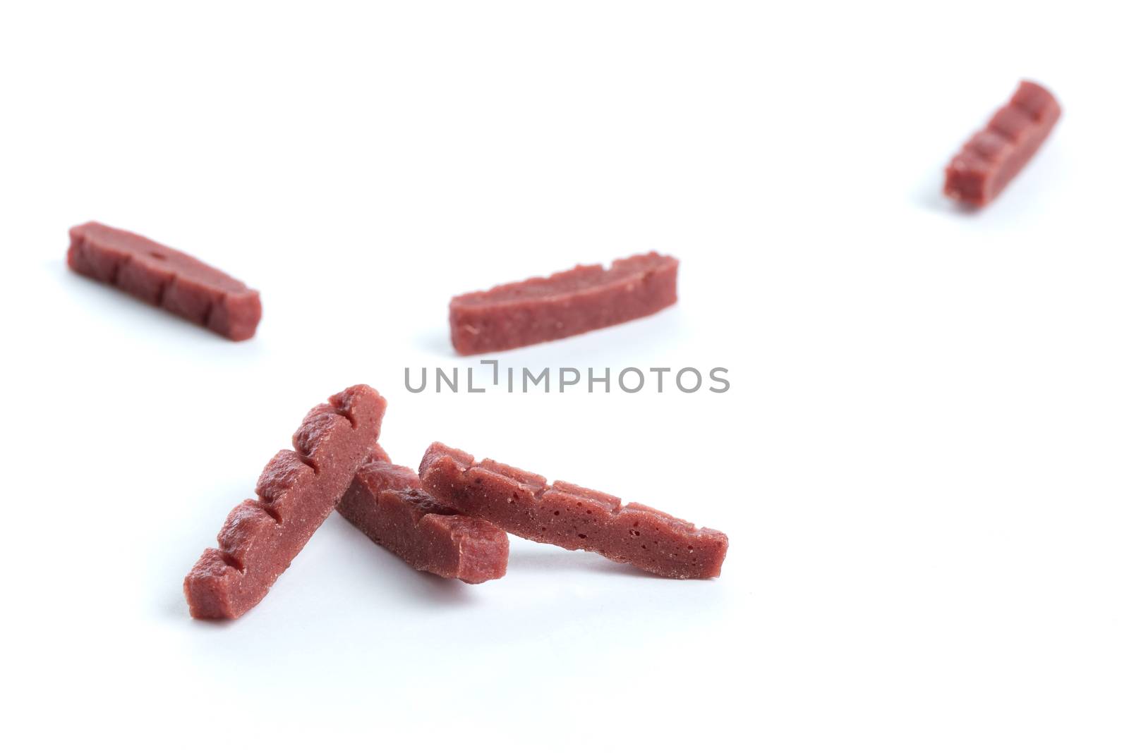 A close up shot of dark red chewy dog treats on a white background.