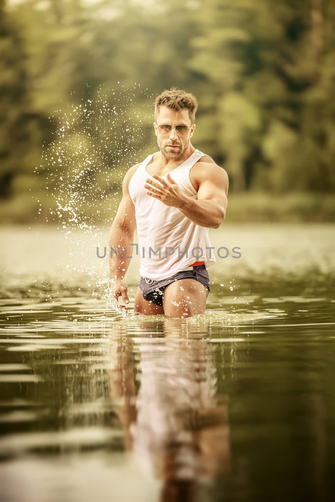 An image of a muscular man in the lake with a white shirt and sunglasses