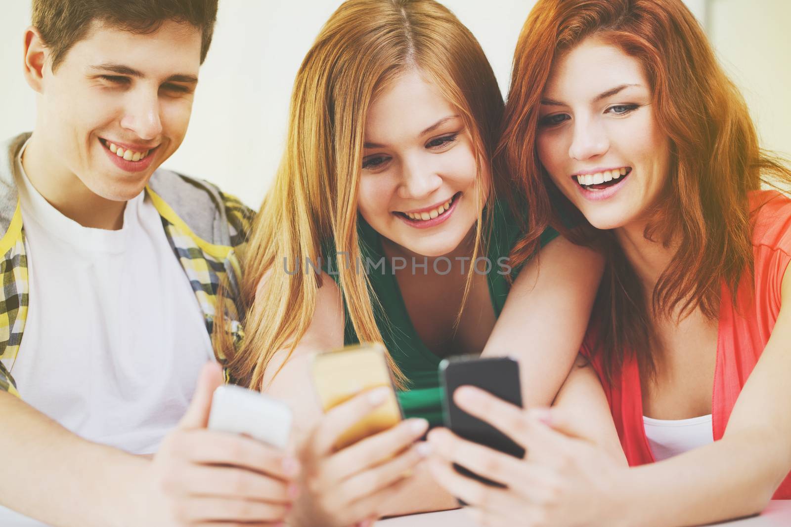 three smiling students with smartphone at school by dolgachov