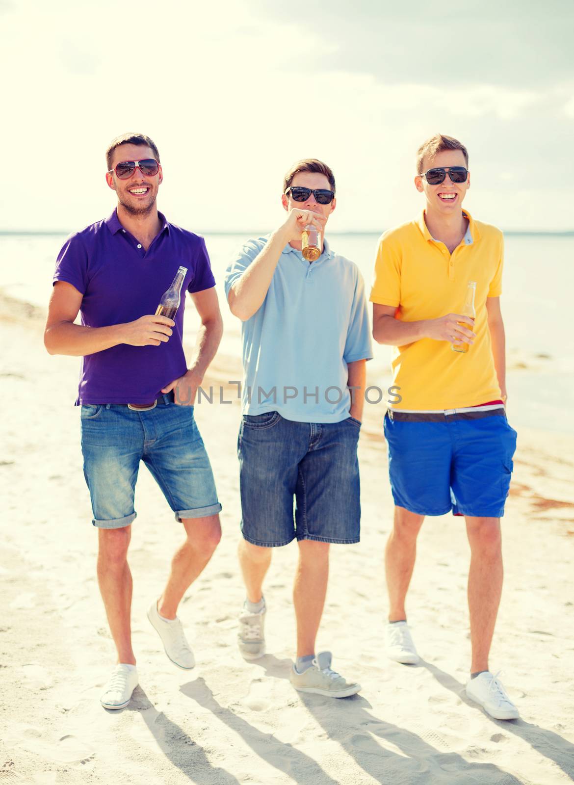 summer, holidays, vacation and people concept - group of male friends having fun on the beach with bottles of beer or non-alcoholic drinks