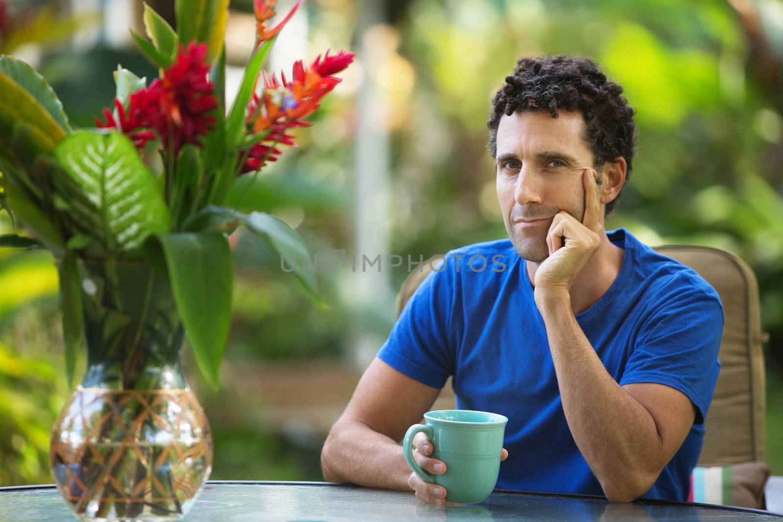 Serious male adult sitting outdoors with hand on chin