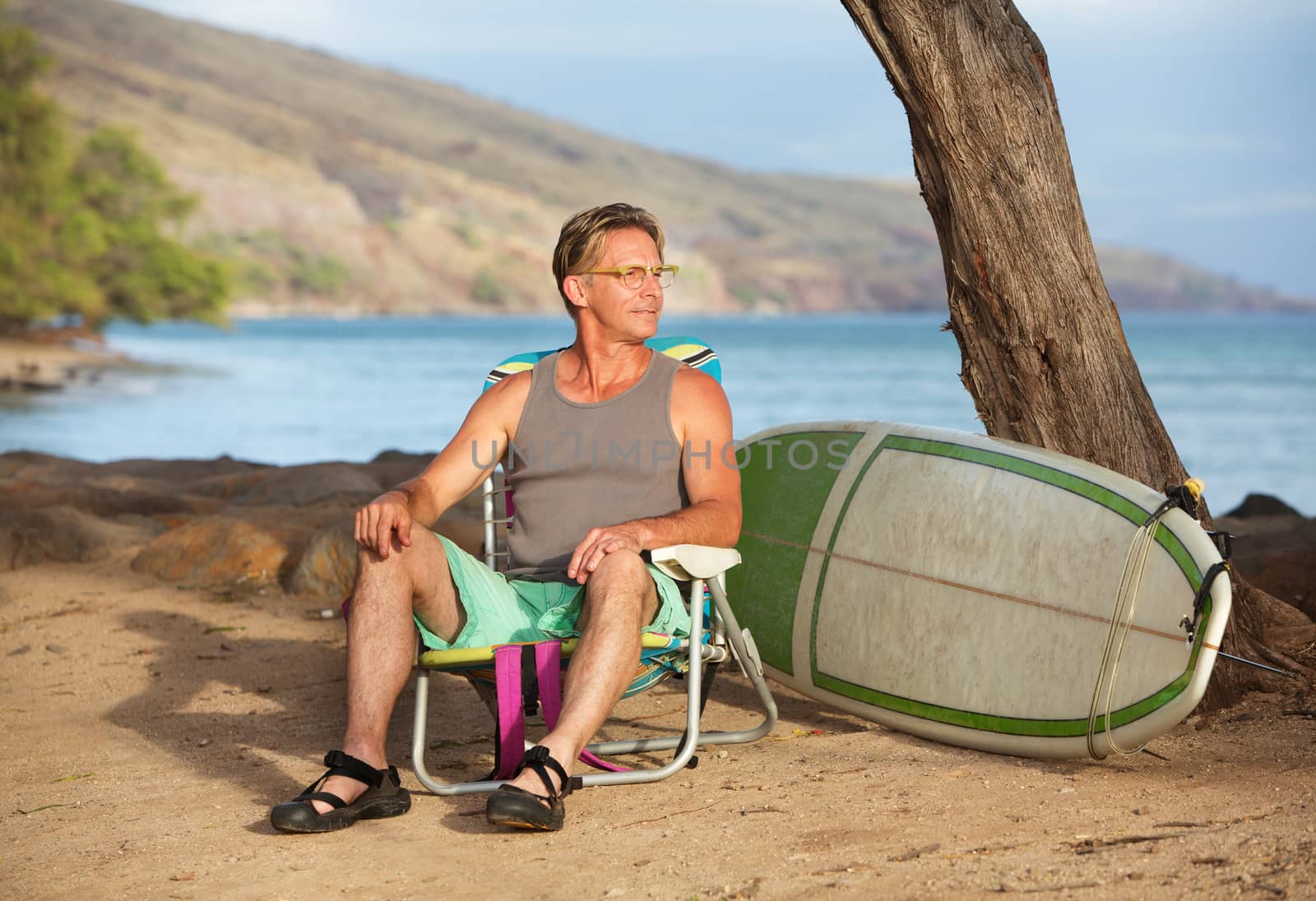Handsome male surfer sitting on beach near his surfboard