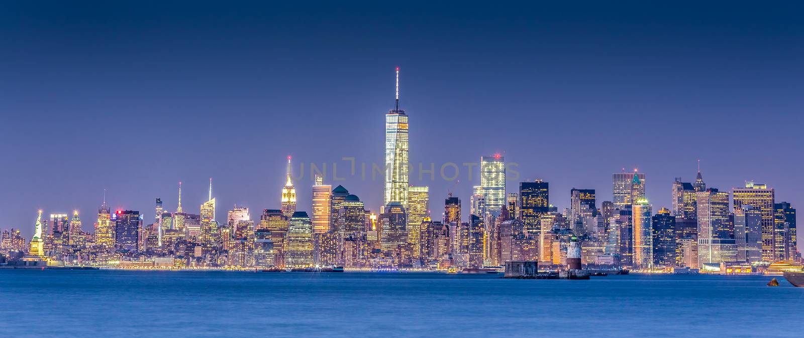 New York City Manhattan downtown skyline at dusk with skyscrapers illuminated over Hudson River panorama. Horizontal composition, copy space.