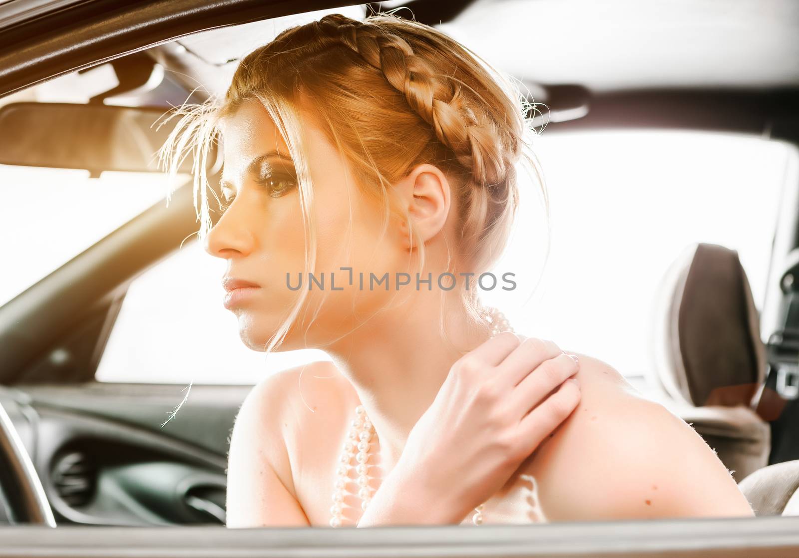 Young Woman in a pearl necklace sat In the drivers seat of her car