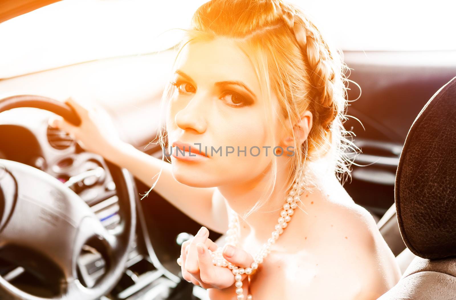 Young Woman in a pearl necklace sat In the drivers seat of her car