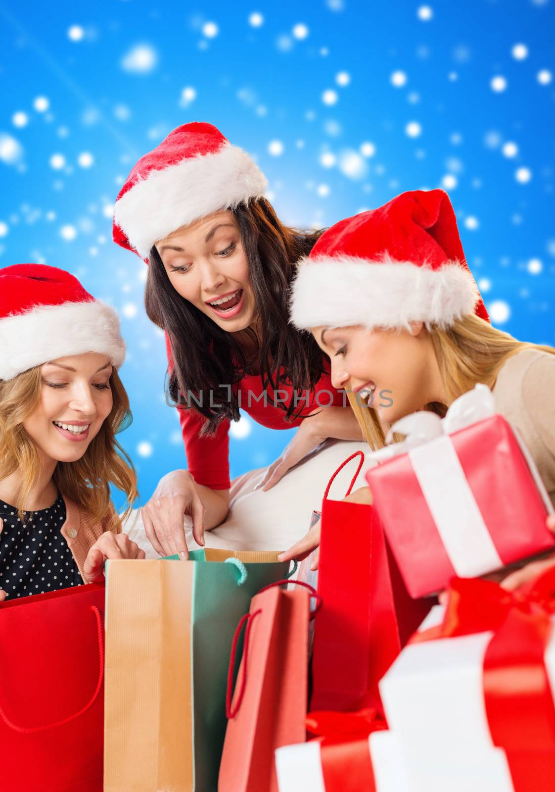 sale, winter holidays, christmas and people concept - smiling young woman in santa helper hat with gifts and shopping bags over blue snowing background