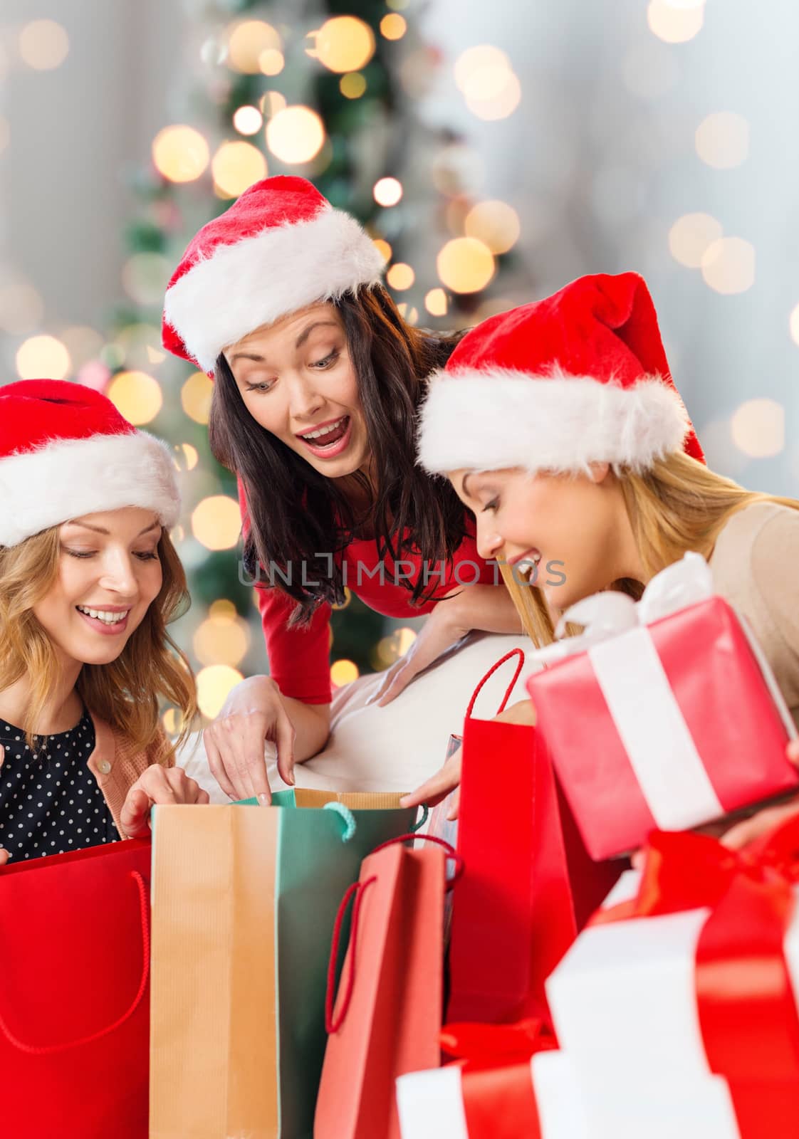 sale, winter holidays and people concept - smiling young woman in santa helper hat with gifts and shopping bags over christmas tree lights background